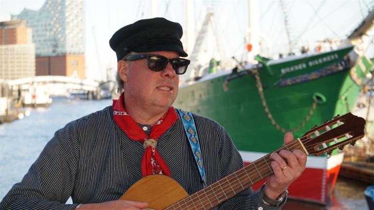 Vor der Hafenkulisse spiel Der Seemannsköpper auf seiner Gitarre